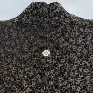 May include: Black and gold fabric with a floral pattern. The fabric has a textured surface and a button in the center.
