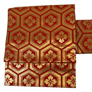 May include: Red fabric with a gold geometric pattern of repeating hexagons and four-leaf flowers.