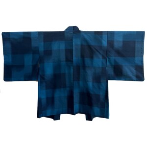 May include: A blue kimono with a plaid pattern. The kimono is a dark blue color with lighter blue squares. The sleeves are wide and the garment is laid flat. The kimono is made of a soft, flowing fabric.