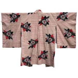 May include: A light pink kimono with a repeating pattern of geometric shapes in black, red, and white. The kimono has long sleeves and a collared neckline. The fabric has a subtle striped texture.