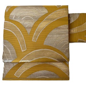 Può includere: Un tessuto giallo e argento con un motivo geometrico di linee curve e archi. Il tessuto ha una texture sottile e un leggero effetto metallizzato.