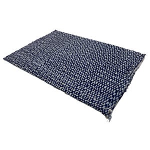 May include: A rectangular woven placemat with a navy blue and white pattern. The placemat has a textured surface and a frayed edge. The weave creates a grid-like design, suitable for kitchen or dining decor.