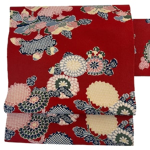 Puede incluir: Una tela roja vibrante con un estampado floral. El diseño presenta grandes flores estilizadas en tonos crema, rosa, azul y verde. La tela probablemente se utiliza para ropa o fines decorativos.