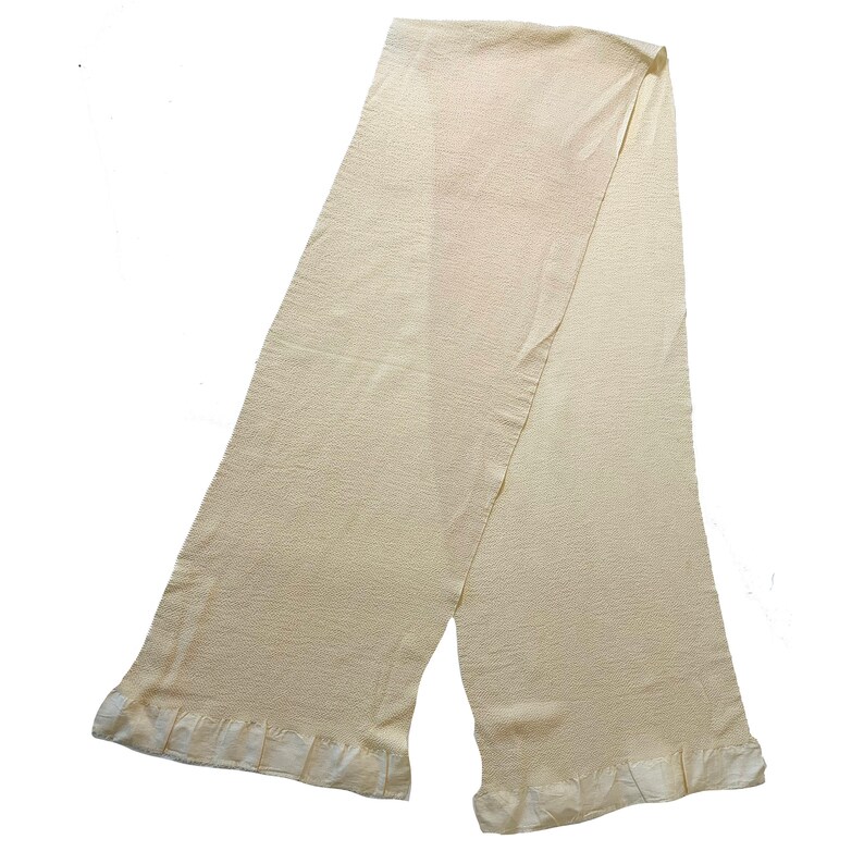 May include: A cream-colored knitted scarf with a ruffled edge.