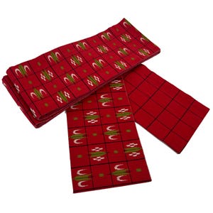 May include: Red fabric with a repeating pattern of white, green, and black geometric shapes. The fabric is folded and arranged in a layered composition. The overall theme is textiles.