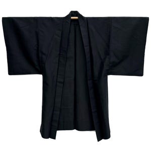 May include: A black kimono-style robe with wide sleeves, hanging open. The robe is made of a solid, dark fabric, and the collar is visible. The garment is displayed against a white background, highlighting its shape and design.