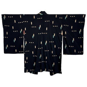 Op de afbeelding: Een zwarte kimono met een herhalend patroon van kleine, abstracte figuren in wit, lichtblauw en perzik. De kimono is uitgespreid, wat de volledige lengte en brede mouwen laat zien. De stof lijkt zacht te zijn.