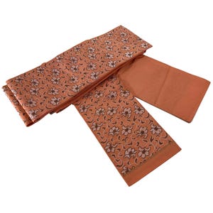 May include: A folded orange fabric sash with a floral pattern. The sash is made of a soft, lightweight material and is perfect for adding a touch of elegance to any outfit.