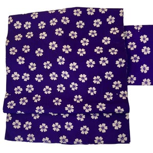 Puede incluir: Tela morada con un patrón floral blanco. La tela está doblada en tres.
