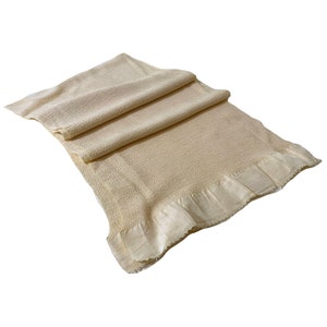 May include: A cream-colored woven throw blanket with a ruffled edge. The blanket is folded and has a soft, textured surface.