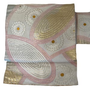 Puede incluir: Una tela blanca con un patrón rosa y dorado de flores estilizadas y formas abstractas. La tela tiene una textura sutil y un brillo ligeramente iridiscente.