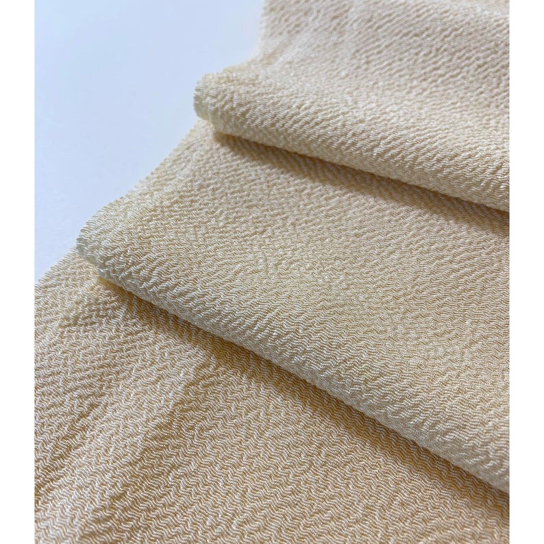 May include: A close-up of a folded piece of off-white fabric with a textured herringbone pattern.