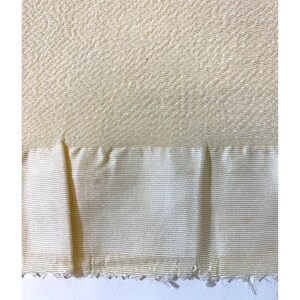 May include: A close-up of a cream-colored fabric with a textured pattern. The fabric has a smooth, silky feel and a subtle sheen. The fabric is folded in half, revealing a slightly different texture on the underside.
