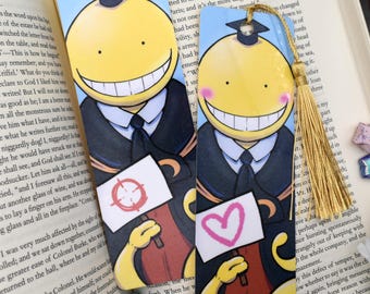 May include: Two anime-style character bookmarks. Each bookmark features a yellow character with a large smile, wearing a graduation cap and holding a sign. One sign has a target, the other a pink heart.