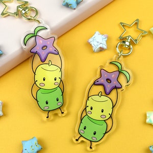 May include: Two colorful acrylic keychain charms featuring a stack of three cartoon characters with a starfish on top. The characters are green, yellow, and green. The charms are attached to gold star-shaped keychains.