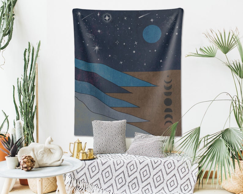 May include: A tapestry with a dark blue background featuring a crescent moon, stars, and a stylized landscape with blue and brown mountains. The tapestry has a fringe border.