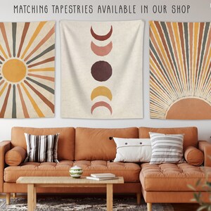May include: Three wall tapestries with a boho aesthetic. The tapestries feature a sun with rays, a moon with phases, and a sun with rays. The tapestries are hung on a white wall above a brown couch.