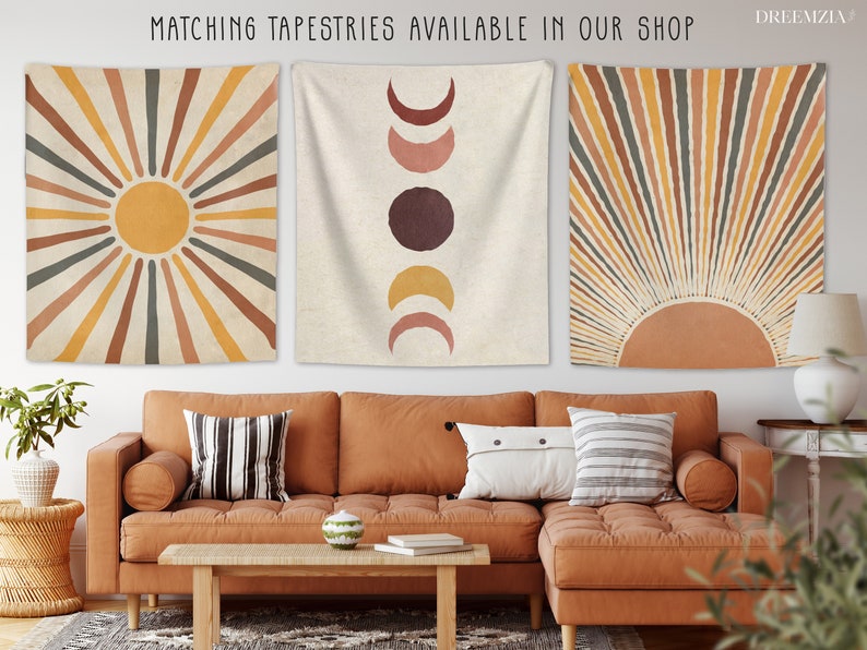 May include: Three wall tapestries with a boho aesthetic. The tapestries feature a sun with rays, a moon with phases, and a sun with rays. The tapestries are hung on a white wall above a brown couch.