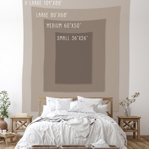 May include: A white bed with a white blanket and pillows, a brown wooden headboard, and two wicker baskets at the foot of the bed. The bed is in front of a wall with a beige tapestry hanging on it. The tapestry has text that reads "X-LARGE 101"x88", "LARGE 80"x68", "MEDIUM 60"x50", and "SMALL 36"x26".