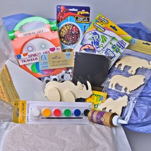 Pu&ograve; includere: Una collezione di materiali per l'artigianato tra cui un kit di arte a spirale, un set di vernici, occhi finti, sagome di animali in legno e un kit di pittura e esposizione di Spider-Man. Gli articoli sono disposti in una scatola con carta velina blu.