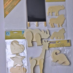 Pu&ograve; includere: Un assortimento di materiali per l'artigianato tra cui una tela bianca tesa, una piccola lavagna nera su un cavalletto di legno e vari ritagli di legno. I ritagli includono forme di animali e altre forme.