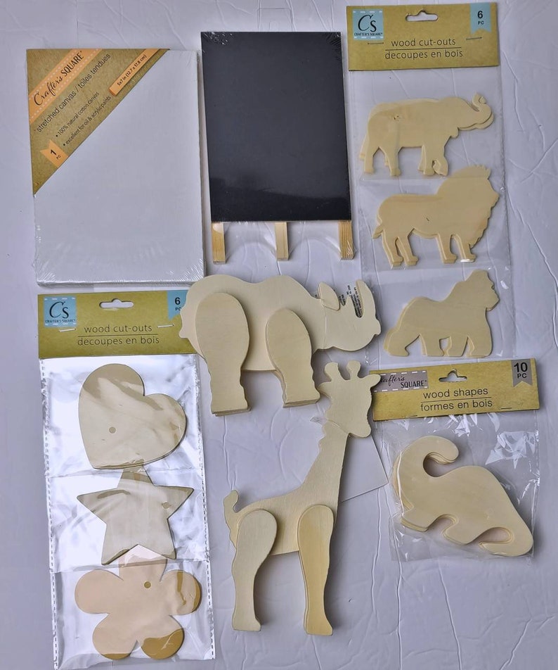 Pu&ograve; includere: Un assortimento di materiali per l'artigianato tra cui una tela bianca tesa, una piccola lavagna nera su un cavalletto di legno e vari ritagli di legno. I ritagli includono forme di animali e altre forme.