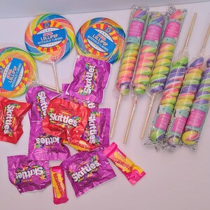 Pu&ograve; includere: Un assortimento di caramelle colorate, tra cui lecca-lecca a spirale con etichette blu, Skittles e lecca-lecca a forma di corno di unicorno. I lecca-lecca hanno spirali color arcobaleno. Gli Skittles sono in confezioni viola e rosse.