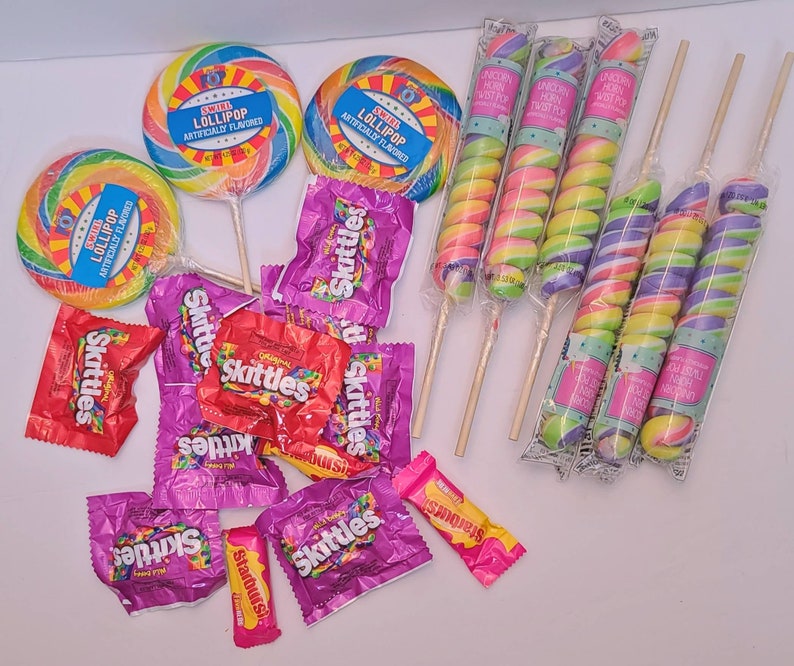 Pu&ograve; includere: Un assortimento di caramelle colorate, tra cui lecca-lecca a spirale con etichette blu, Skittles e lecca-lecca a forma di corno di unicorno. I lecca-lecca hanno spirali color arcobaleno. Gli Skittles sono in confezioni viola e rosse.