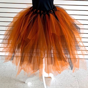 May include: A layered tulle skirt featuring alternating strips of vibrant orange and deep black fabric. The skirt has a gathered, elasticized waistband and a voluminous, multi-layered design that creates a full, flared silhouette with sheer texture.