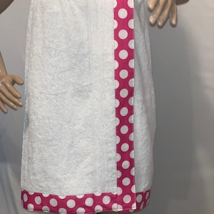 Puede incluir: Envoltura de baño blanca con un ribete de lunares rosa y blanco. El ribete está en el lateral y en la parte inferior de la envoltura.