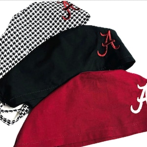 May include: Three scrub caps stacked together. The top cap features a black and white houndstooth pattern with a red embroidered letter A. The middle cap is solid black with a red embroidered letter A. The bottom cap is solid maroon with a white embroidered letter A.