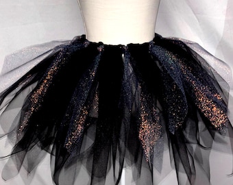 May include: A layered tutu skirt made of black tulle fabric. The skirt features alternating panels of solid black tulle and black tulle with a shimmering, glittery copper-toned finish that catches the light, creating a voluminous and textured appearance.