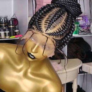 May include: A black braided wig with a lace front and a high bun. The wig is on a mannequin head with a gold finish.