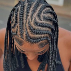 May include: Close-up of a person's head featuring intricate black braids styled in a geometric pattern. The braids are neatly sectioned and flow in a wave-like design, with some braids hanging down.