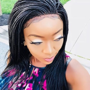 May include: A black braided wig with a lace front. The wig is styled in small, thin braids that are parted in the middle and fall straight down.