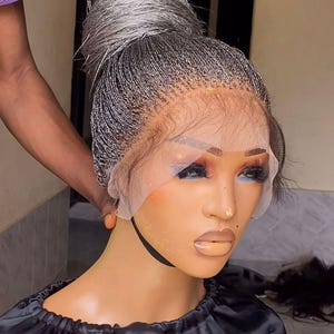 May include: A gray wig with a braided style, pulled back into a high bun. The wig is on a mannequin head with a black fabric covering the shoulders.
