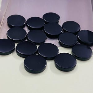 Könnte beinhalten: Eine Ansammlung von zwölf polierten, runden, schwarzen Edelsteinen. Die Steine sind in einer silbernen Schale angeordnet, jede mit einer glatten, reflektierenden Oberfläche. Die Edelsteine sind gleichmäßig groß und geformt.