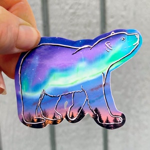 May include: A sticker of a polar bear with a silhouette of the aurora borealis in the background. The aurora is a vibrant mix of purple, green, and blue.