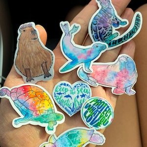 May include: A set of nine colourful stickers featuring various animals and nature-themed designs. The stickers include a capybara, a seal, a walrus, a turtle, a heart with the text "keep the sea plastic free", and a circle with the text "protect what you love".