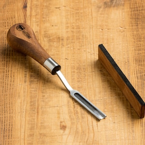 May include: A wooden handled leather carving tool with a metal blade and a black leather sharpening strop.
