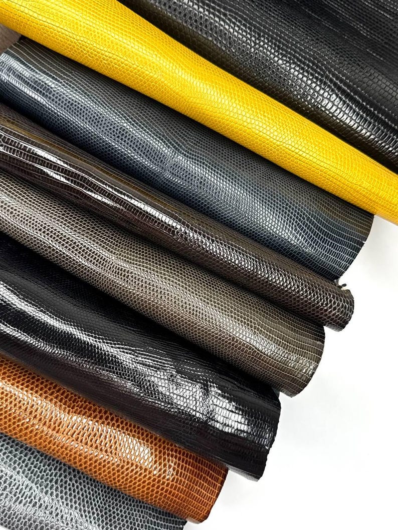 Puede incluir: Una colecci&oacute;n de ocho muestras de cuero de diferentes colores, cada una con un patr&oacute;n texturizado &uacute;nico que se asemeja a la piel de serpiente. Los colores incluyen amarillo, gris, marr&oacute;n y negro.