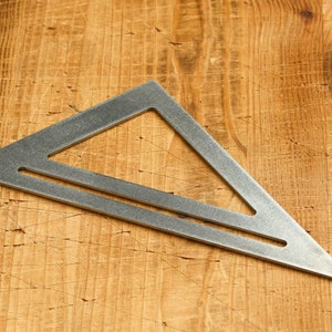 Op de afbeelding: Een zilveren metalen driehoeksliniaal met een rechte rand en een gat in het midden. De liniaal ligt op een houten oppervlak.