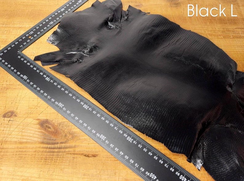 Puede incluir: Cuero negro con un patr&oacute;n texturizado y escamoso. El cuero se coloca plano sobre una superficie de madera con una regla para la escala.