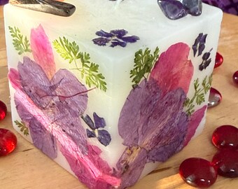 A square shaped white candle with Purple Azaleas, Pink Peony petals, small flowers and foliage