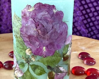 A Pinkish Purple Rose and Rosebuds with Green Foliage on a Light Green Scented Candle