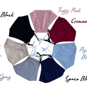 May include: A collection of face masks in various colors, including Onyx Black, Taffy Pink, Crimson Red, Pigeon Blue, and Space Blue. Each mask has adjustable white ear loops and is displayed against a white background. The names of the colors are written in cursive.