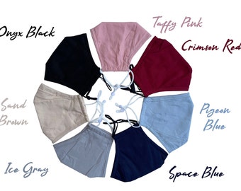 Könnte beinhalten: Eine Auswahl an Gesichtsmasken in verschiedenen Farben, darunter Onyx Black, Taffy Pink, Crimson Red, Pigeon Blue und Space Blue. Jede Maske hat verstellbare weiße Ohrschlaufen und wird vor einem weißen Hintergrund präsentiert. Die Farbbezeichnungen sind kursiv geschrieben.
