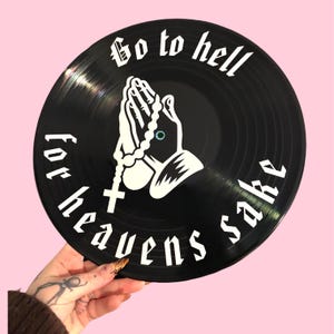 May include: Black vinyl record featuring white text and a graphic of praying hands with a rosary. The record's text reads "Go to hell for heavens sake". A unique decorative item.