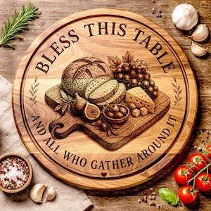 Puede incluir: Una tabla redonda de madera para servir con el texto grabado "Bless This Table And All Who Gather Around It". La tabla presenta una tabla de cortar con pan, queso, uvas, higos y aceitunas. Ajo, tomates y ramitas de romero están dispuestos alrededor de la tabla.