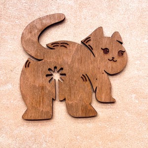 May include: Wooden cat-shaped cutout with a playful design. The cat is depicted in a standing pose with a curved tail and a star-shaped cutout. The cat has a smiling face and is made of light brown wood.